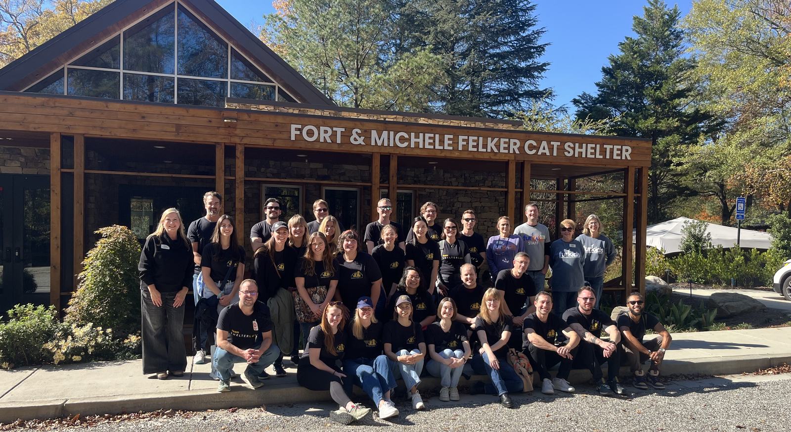Around thirty five Shelterluv employees in Team Shelterluv shirts, posed together outside the Fort and Michele Felker Cat Shelter on a clear autumn day.